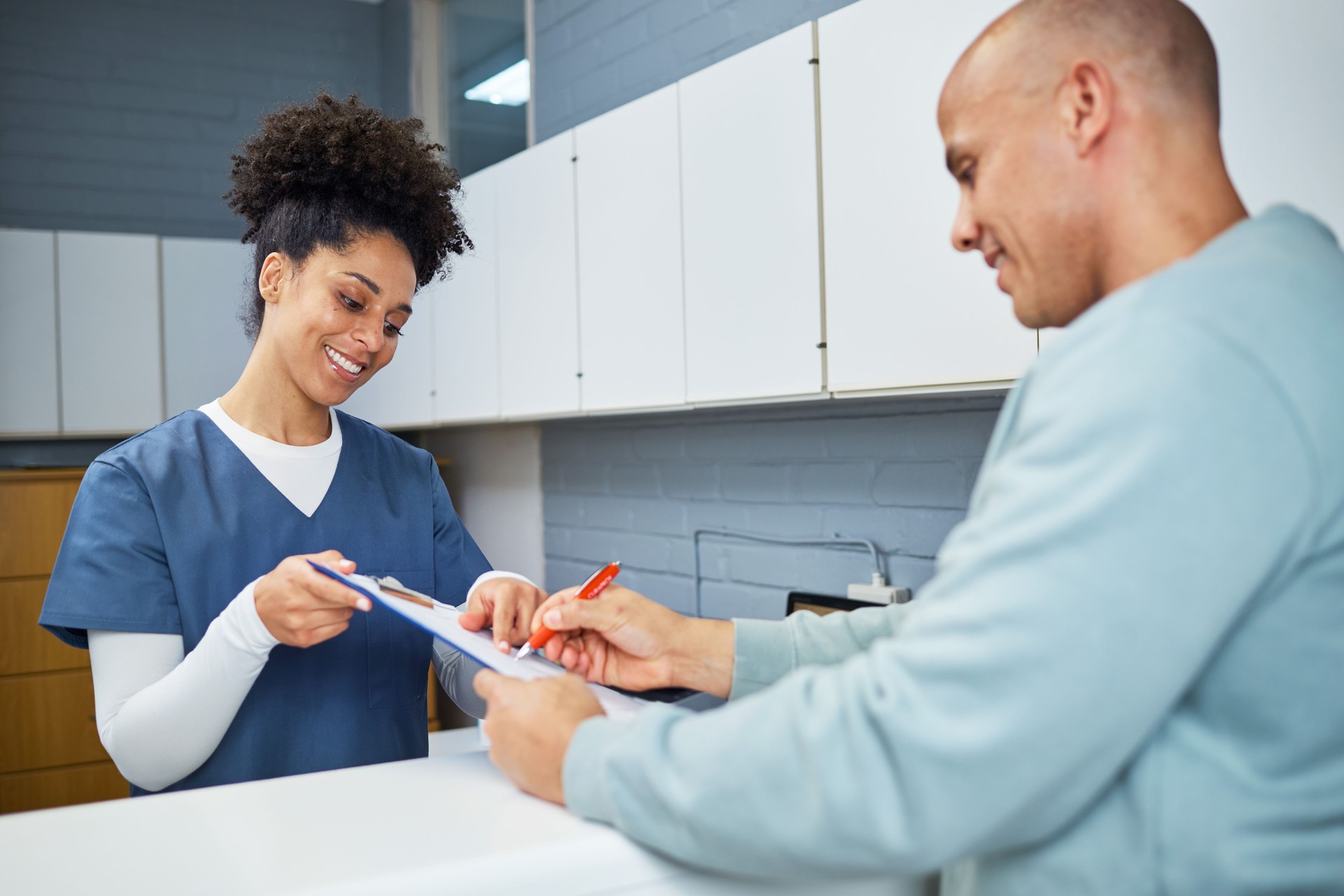Smiling Healthcare Professional Assisting Patient with Forms at Reception Desk in Modern Clinic